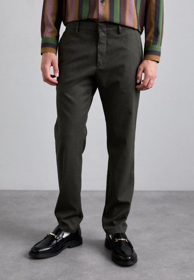 Pantalons ajustés vert olive en tissu texturé, avec un design à front plat et des poches latérales. Associés à des mocassins noirs brillants.