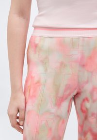 Zbliżenie osoby noszącej spodnie z wysokim stanem o abstrakcyjnym wzorze w kolorach różowym, beżowym i zielonym oraz blady różowy top bez rękawów.