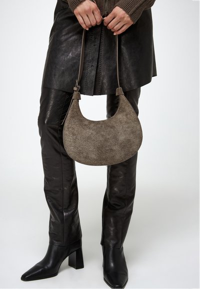 Borsa hobo in suede marrone chiaro con forma curva, manico corto e texture sottile. Abbinata a pantaloni in pelle nera e stivali con tacco.