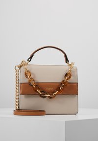 Bolso de mano de cuero beige con una franja de cuero marrón, herrajes dorados y un acento de cadena transparente gruesa. Incluye una correa de hombro desmontable.