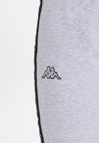 Grå joggers i mjukt tyg, med slim fit, svarta sidostråkar och en broderad logotyp på vänster lår.