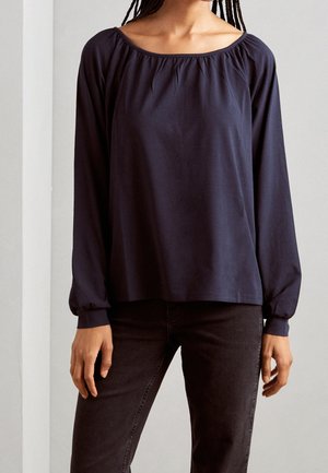 Donkerblauwe blouse met lange mouwen, brede halslijn, gerimpelde details op de schouders en een losse pasvorm. De stof lijkt glad en lichtgewicht.