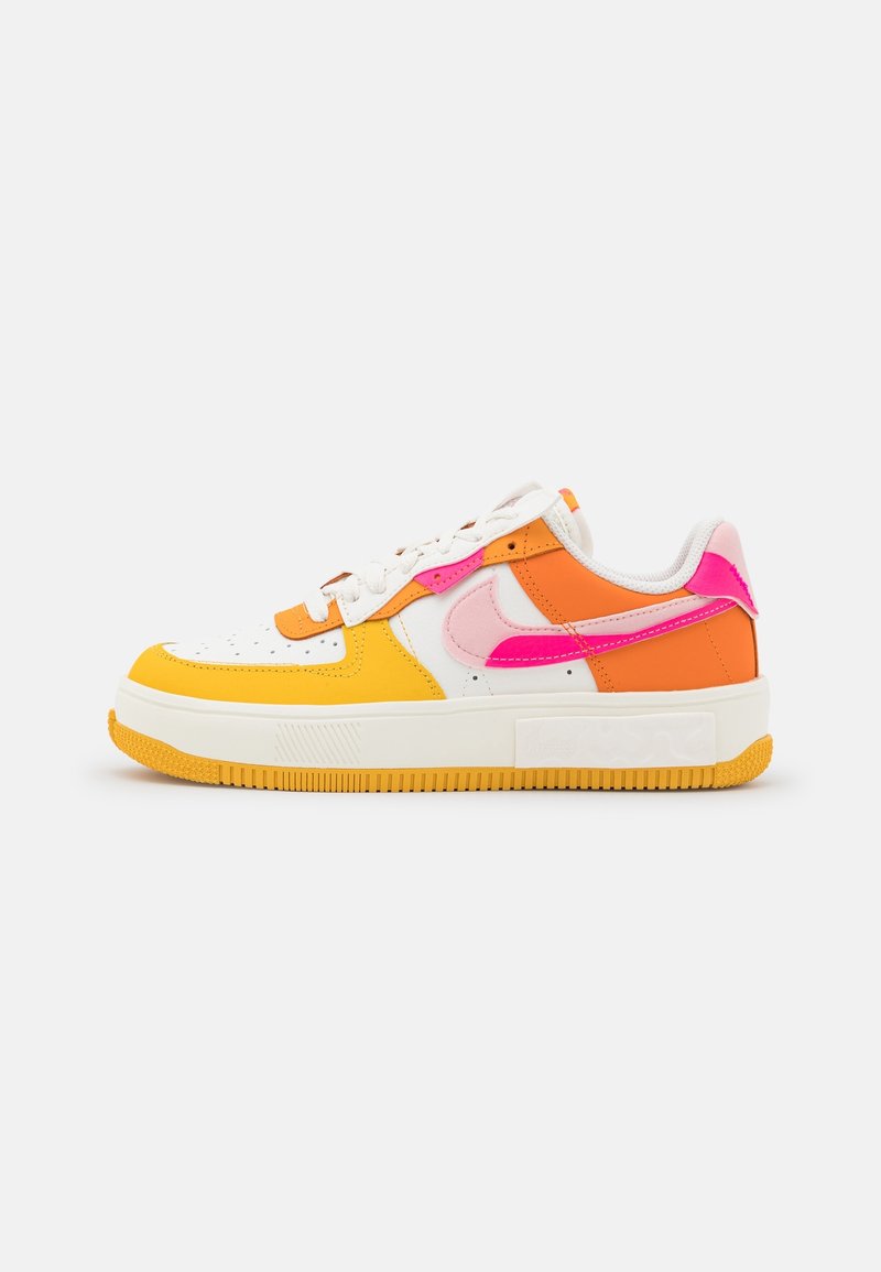 Baskets basses avec base blanche, panneaux jaunes et orange, logos Nike roses et rose vif, lacets blancs et semelle extérieure jaune.