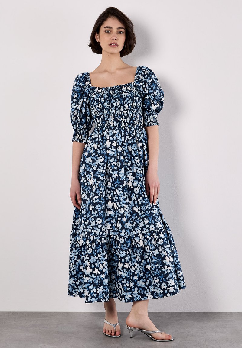 Robe maxi florale en bleu foncé et blanc, dotée de manches bouffantes, d'un buste smocké et d'un ourlet inférieur en couches pour plus de volume.