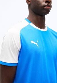 Άνδρας που φοράει μπλε και λευκή αθλητική φανέλα Puma, εμφανίζοντας τον άνω κορμό και το λογότυπο Puma στο στήθος.