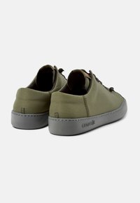 Zapatillas de tela verdes con suelas de goma gris, con costuras mínimas y cordones redondos. Diseño limpio apto para el uso diario.