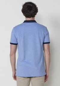 Gai�šs zils īsais piedurkņu polo krekls ar teksturētu audumu, tumši zila apkakle un aproces. Tam ir taisna apakšmala un sānu spraugas.