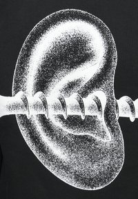 Μαύρο t-shirt με γραφιστικό σχέδιο ενός μεγάλου αυτιού και ενός βιδωτού εξαρτήματος, σε λευκό χρώμα με υφή σπασμένου. Το σχέδιο είναι κεντρικά τοποθετημένο.