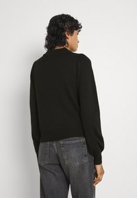 Maglione di colore verde scuro lavorato a maglia, con scollatura rotonda, maniche a sbuffo e orlo a coste. Abbinato a jeans grigi a vita alta.