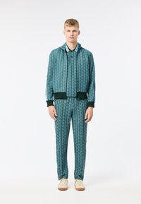 Träningsjacka och byxor i teal med ett geometriskt mönster, med ribbade muddar och krage, dragkedja fram och sidostripes. Sneakers ingår.