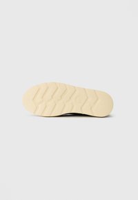 Shoe sole with beige zigzag tread pattern and embossed logo on a plain white background.