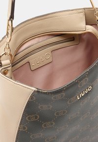 Borsa a mano in pelle beige e verde scuro con esterno testurizzato, dettagli in metallo dorato, etichetta con logo e interno in tessuto rosa con tasca con cerniera.