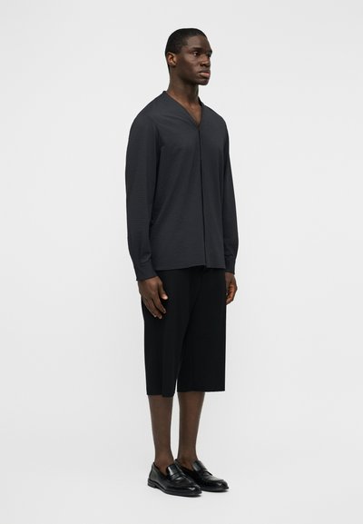 Μαύρο πουκάμισο μακρυμάνικο με V-λαιμόκοψη, υφή υφάσματος, σε συνδυασμό με μαύρο σορτς μέχρι το γόνατο και μαύρα μοκασίνια. Απλό, μοντέρνο σιλουέτα.