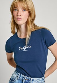 T-shirt à manches courtes bleu marine avec le logo "Pepe Jeans London" en blanc. Tissu en coton doux, coupe classique, associé à un jean en denim clair.