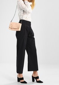 Top bianco in pizzo con maniche lunghe, pantaloni neri a vita alta e a gamba larga, mules nere con tacco, borsa a tracolla rosa con ritagli floreali e tracolla a catena.