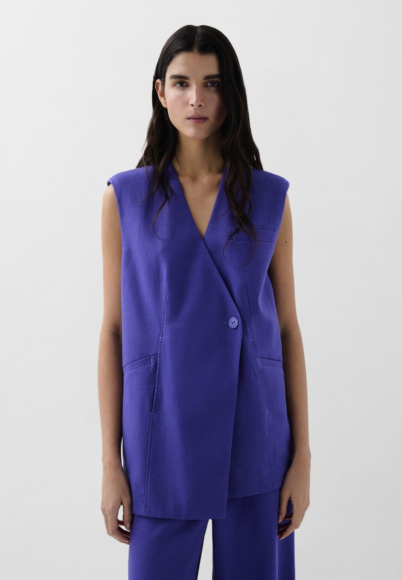 Violet ærmeløs blazer med dyb V-hals, enkelt knaplukning og to forlommer. Fremstillet af glat stof med minimal tekstur.