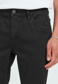 Črne jeans hlače iz denima z rahlo teksturo, z sprednjim žepom, gumbom za zapiranje in vidnimi šivi ob šivih.