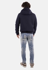 Felpa con cappuccio colore blu navy con finitura texture, abbinata a jeans azzurri strappati e sneakers marroni e bianche.