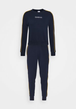 Navyblåt Reebok træningssæt med gule striber langs ærmer og bukseben, som inkluderer en sweat-shirt med rund hals og smalle joggebukser.