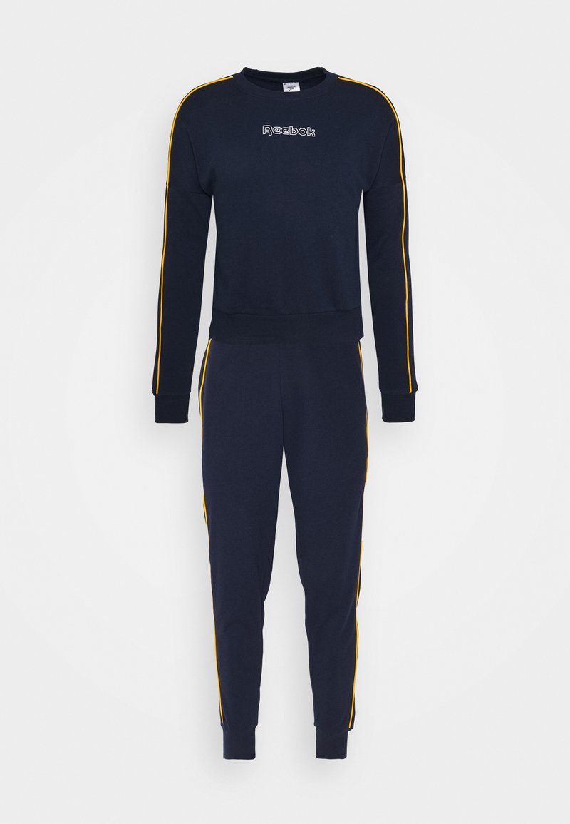 Survêtement Reebok bleu marine avec des bandes jaunes le long des manches et des jambes, comprenant un sweat à col rond et un pantalon de jogging fuselé.