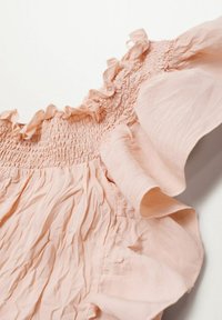 Vaaleanpunainen olkaimeton paita, jossa on kootut yksityiskohdat, frillimuotoilu ja teksturoitu kangas. Paita esittelee pehmeitä, virtaavia laskoksia ja lempeitä taitoksia.