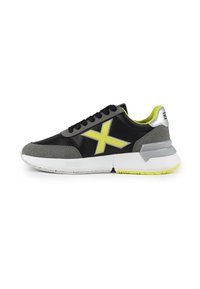 Baskets noires et grises avec une tige texturée, accents jaune néon et une semelle chunky blanche. Présente un logo "X" jaune distinctif.