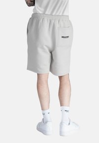 Pantaloni corti grigi chiari in cotone misto, con elastico in vita e una tasca posteriore con logo "MULTIPLY". Abbinati a sneaker bianche e calze.