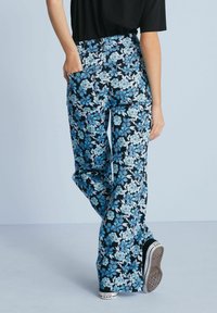 Rozšířené kalhoty s květinovým vzorem v modré a bílé na černém pozadí, s bočními kapsami a vysokým pasem, doplněné teniskami.