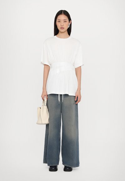 Vit oversized t-shirt med en blank midjeband, parat med vida bleka denimjeans och en liten handväska i krämfärg.