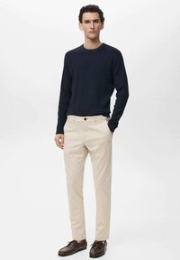 Navy ribbed long-sleeve sweater, beige trousers with front pockets, and brown lace-up shoes. Smooth texture, tailored fit, simple design.