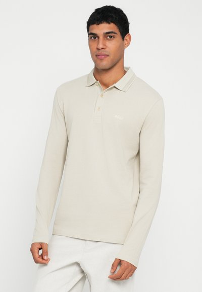 Polo à manches longues beige en tissu texturé, doté d'un col, d'une patte à trois boutons et d'un logo discret sur la poitrine.