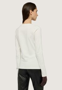 Top blanco de manga larga con escote redondo, textura suave y silueta ajustada; combinado con pantalones de cuero negros y guantes oscuros.