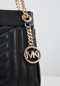 Borsa a tracolla nera in pelle trapuntata con catena dorata e charm rotondo in oro con il logo di Michael Kors appeso al manico.