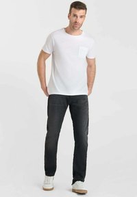 T-shirt blanche à manches courtes avec poche, associée à un jean gris foncé et des baskets blanches. Tissu lisse, design simple et coupe classique.