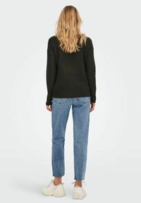 Pull en maille noir, jean bleu clair et baskets blanches. Le pull a une coupe ample ; le jean a un ourlet brut. Design simple et décontracté.