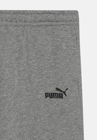 Pelēki auduma joggeri ar mīkstu tekstūru, elastīgu jostasvietu un melnu Puma logotipu apakšējā kājā.