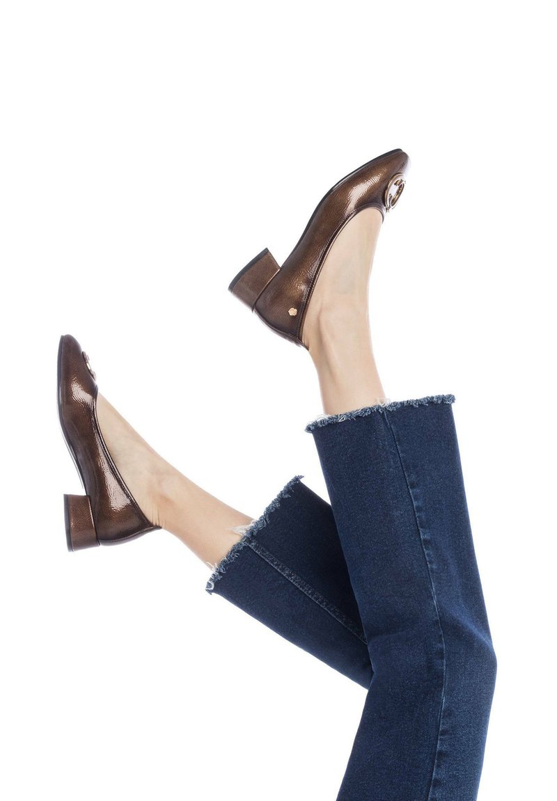 Zapatos de charol marrón con punta redonda y tacón cuadrado, con un acento en tono dorado en el costado. Combinados con denim deshilachado.