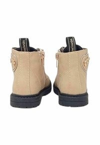Stivaletti beige con finitura in suede liscia, suole in gomma nera, cerniere laterali e un emblema a forma di cuore decorativo sul tacco esterno.