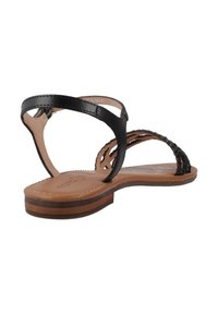 Zwart leren sandaal met gevlochten banden en een bruine zool. Heeft een platte ontwerp met minimale hardware en een gladde textuur.