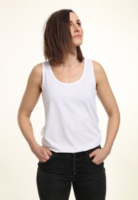 Witte katoenen tanktop met een ronde hals, gecombineerd met hooggewaiste zwarte jeans met een sluiting van vijf knopen en voorzakken.