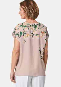 Kurzärmlige Bluse aus weichem pinkfarbenem Stoff mit floralem Muster in Weiß und Gelb, mit einem runden Ausschnitt und lockerer Passform.