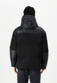 Sort pufferjakke med en polstret hætte, der har en blanding af matte og shiny teksturer, horisontale sømme og en afslappet pasform.
