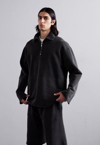Mørk grå zip-up genser i myk stoff, med høy krage, løs passform og lange ermer. Kombinert med matchende shorts.