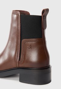 Brown leather boot with black elastic side panel, rounded toe, short heel, and branded accent on the side. Smooth texture.