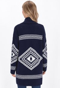 Cardigan lavorato a maglia blu navy con motivi geometrici bianchi e colletto scialle. Presenta maniche lunghe e un design dalla vestibilità comoda.