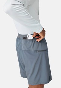 Shorts de sport gris avec un détail de poche en mesh, dotés d'un compartiment zippé. Le tissu est léger avec une texture lisse.