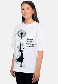 Witte T-shirt met korte mouwen met een ontwerp van een paardenbloem en silhouet, met de tekst "Verander jezelf om de wereld te veranderen" in zwart.