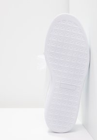 Bílá teniska s texturovanou gumovou podrážkou se vzorem hvězd. Vrchní část je z hladkého syntetického materiálu s minimálními zdobeními.