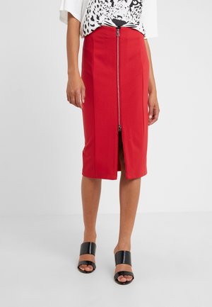 Mujer vistiendo una falda lápiz roja hasta la rodilla con una cremallera frontal central y una camiseta blanca con estampado de leopardo en blanco y negro.