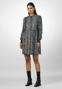 Leopardi-kuosiset mekko, jossa on korkea kaulus, napitettavat etuosat ja pitkät puffihihat. Kangas on sileä, yhdistettynä mustiin nilkkasaappaisiin.